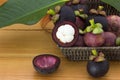 Ripe mangosteens Garcinia mangostana with green leaves in a basket on the wooden table