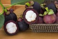 Ripe mangosteens Garcinia mangostana with green leaves in a basket on the wooden table