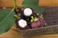 Ripe mangosteens Garcinia mangostana with green leaves in a basket on the wooden table