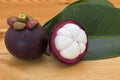 Ripe mangosteens or half mangosteen with green leaves on a wooden table