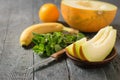 Ripe melon pieces on a clay bowl, banana, mint, orange and knife on a wooden table. Royalty Free Stock Photo