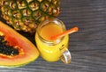 Ripe organic papaya and pineapple tropical fruit cut in half and fresh juice in a glass jar on old wooden background. Royalty Free Stock Photo