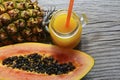 Ripe organic papaya and pineapple tropical fruit cut in half and fresh juice in a glass jar on old wooden background. Royalty Free Stock Photo