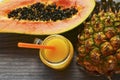 Ripe organic papaya and pineapple tropical fruit cut in half and fresh juice in a glass jar on old wooden background. Royalty Free Stock Photo