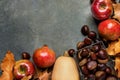 Ripe Organic Red Glossy Apples Pomegranates Chestnuts in Wicker Basket Dry Autumn Leaves Scattered on Dark Stone Background. Royalty Free Stock Photo