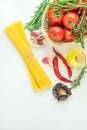 Ripe Organic Tomatoes Herbs Rosemary Thyme in Wicker Basket. Spaghetti Olive Oil in Bottle Dried Hot Peppers Garlic on White Table Royalty Free Stock Photo