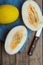 Ripe organic yellow melons, halved and whole on dark plank wood background, pulp and seeds, blue linen napkin, knife, top view Royalty Free Stock Photo