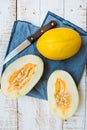 Ripe organic yellow melons, halved and whole on white plank wood garden table, pulp and seeds, blue linen napkin, knife