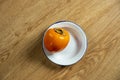 Ripe persimmon on white plate with blue edge on wooden table.