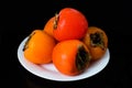 Ripe persimmons in a plate on a black background. Royalty Free Stock Photo