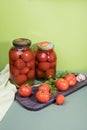 Ripe pickled tomatoes in jars . Fresh tomatoes with garlic and herbs are on the cutting Board.