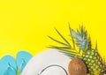 Ripe pineapple coconut on green palm leaf white straw hat blue slippers on bright yellow solid background. Summer vacation fun