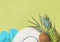 Ripe pineapple coconut on green palm leaf white straw hat blue slippers on pastel chartreuse background. Summer vacation fun