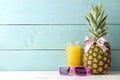 Ripe pineapple fruit with a pink bow, sunglasses and pineapple juice on a blue wooden background. place for text