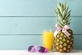 Ripe pineapple fruit with a pink bow, sunglasses and pineapple juice on a blue wooden background. place for text