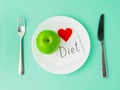 Ripe raw juicy green Apple, red heart, slip of paper with inscription diet on a white plate, fork, knife on a bright turquoise bl Royalty Free Stock Photo