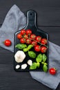 Ripe red cherry tomatoes, basil leaves and garlic on a marble cutting board on black wooden table, top view Royalty Free Stock Photo