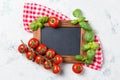 Ripe cherry tomatoes and fresh basil leaves on stone table with chalkboard, cooking ingredients top view Royalty Free Stock Photo