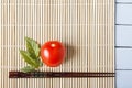 Ripe red fresh tomato and chopsticks on bamboo mat. Chinese and japanese kitchen concept. Top view with copy space Royalty Free Stock Photo