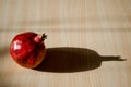 Ripe red fruit pomegranate on a light striped wooden table under the direct rays of the sun and hard long shadow Royalty Free Stock Photo