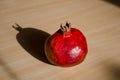 Ripe red fruit pomegranate on light wooden table under the direct rays of the sun and a hard long shadow, side view Royalty Free Stock Photo