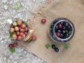 Ripe red gooseberries and leaves lie in a white metal mug on the background of burlap. Cherries in a glass jar next Royalty Free Stock Photo