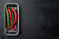 Ripe Red and green chili pepper, in plastic tray, on black background, top view flat lay  , with copyspace  and space for text Royalty Free Stock Photo