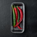 Ripe Red and green chili pepper, in plastic tray, on black background, top view flat lay Royalty Free Stock Photo