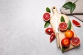 Ripe red oranges, green leaves and wooden board with knife on light table, flat lay. Space for text Royalty Free Stock Photo