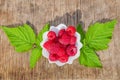 Ripe red raspberries in a white plate on the table on a background of green leaves, Royalty Free Stock Photo