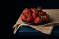 Ripe red strawberries in a black plate on burlap and dark blue wooden background. Sweet dessert from fresh berries on the table Royalty Free Stock Photo