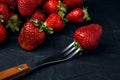 Ripe red strawberries with fork on a dark blue background. Sweet fresh berries on table Royalty Free Stock Photo