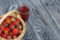 Ripe red strawberries in a wicker basket. Nearby is an open can of strawberry jam. Against the background of pine boards painted Royalty Free Stock Photo