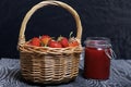 Ripe red strawberries in a wicker basket. Nearby is an open can of strawberry jam. Against the background of pine boards painted Royalty Free Stock Photo