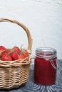 Ripe red strawberries in a wicker basket. Nearby is an open can of strawberry jam. Against the background of pine boards painted Royalty Free Stock Photo