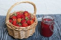 Ripe red strawberries in a wicker basket. Nearby is an open can of strawberry jam. Against the background of pine boards painted Royalty Free Stock Photo