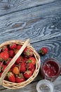 Ripe red strawberries in a wicker basket. Nearby is an open can of strawberry jam. Against the background of pine boards painted Royalty Free Stock Photo