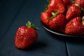 Ripe red strawberry and group of strawberries in a black plate on a dark blue wooden background. Dessert from fresh berries on the Royalty Free Stock Photo