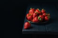 Ripe red strawberry and group of strawberries in a black plate on a dark blue wooden background. Sweet dessert from fresh berries Royalty Free Stock Photo