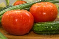 Ripe red tomatoes, green cucumbers, green onion feathers are covered with large drops of water, composition on a wooden Royalty Free Stock Photo