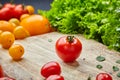 Ripe cherry tomato on a wooden cutting board surrounded by lettuce, basil leaves and yellow tomatoes