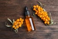 Ripe sea buckthorn and bottle of essential oil on wooden table, flat lay