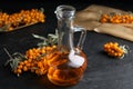 Ripe sea buckthorn and jug of essential oil on black table