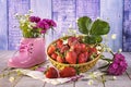 Ripe strawberries in a basket, a bouquet of wild flowers in a pink shoe on a wooden background.