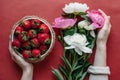 Top view of strawberries in bowl on red background bouquet of peonies Royalty Free Stock Photo