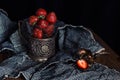Ripe strawberries in old glass holder on dark rough fabrics background.