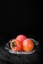 Ripe sweet persimmon fruit on silver tray, black background