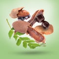 Ripe tamarind pods, seeds and leaves falling on light green background