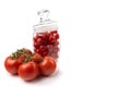 Ripe tomatoes on a twig and a glass jar filled with cherries, close-up, white background, horizontal view Royalty Free Stock Photo