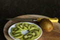 Ripe whole kiwi fruits and slices of kiwi fruits on chopping board with knife with black wooden surface. Selective focus Royalty Free Stock Photo